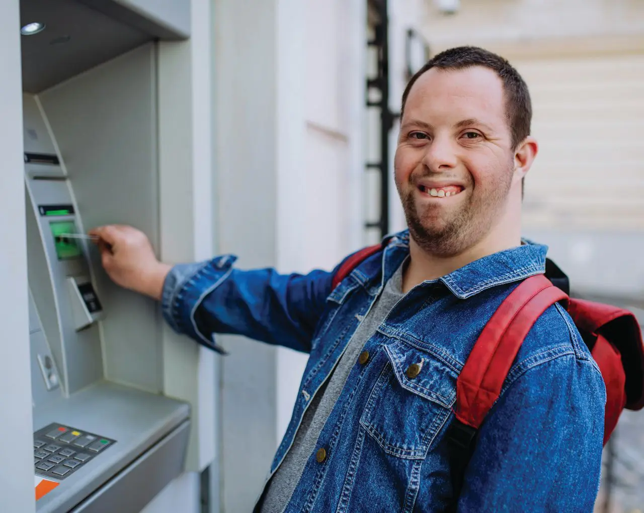 Man with Down syndrome using an ATM and smiling.