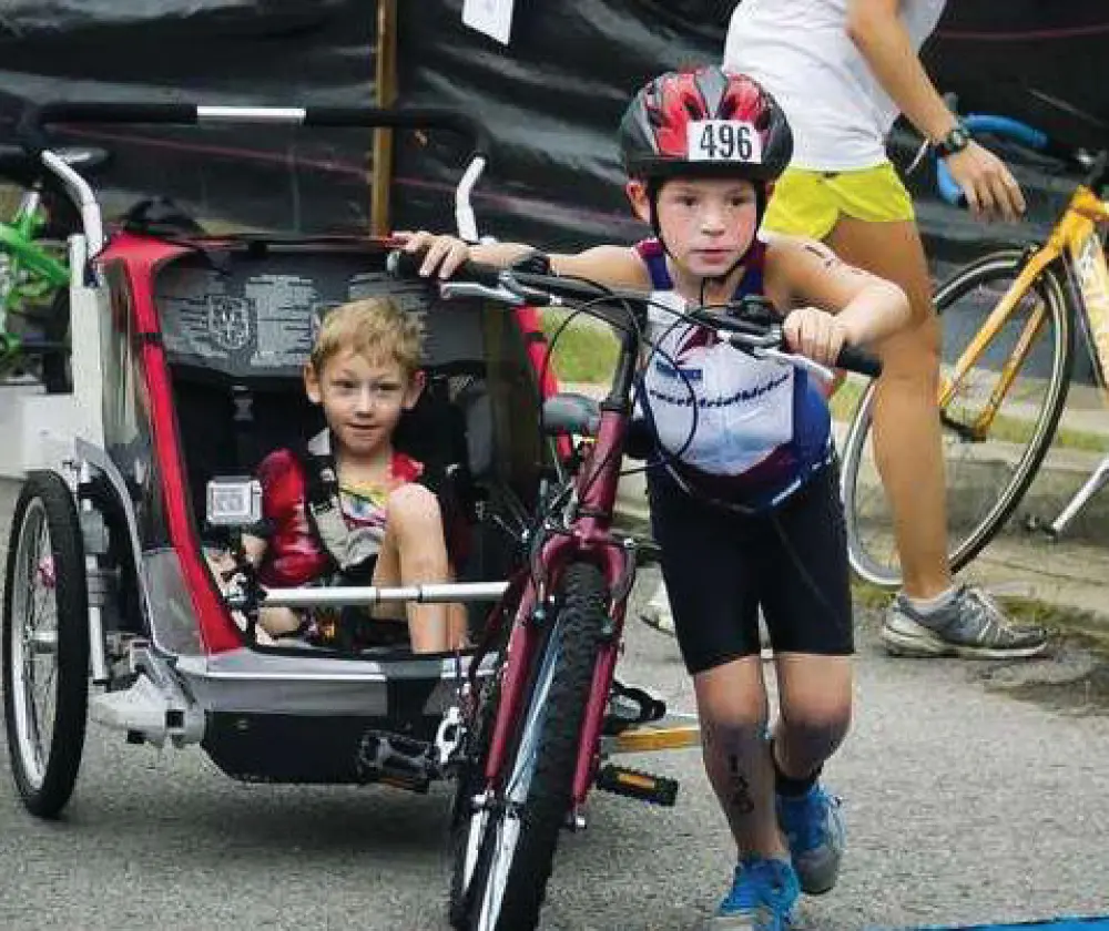Two children in a race, one on a bicycle and one in a stroller.