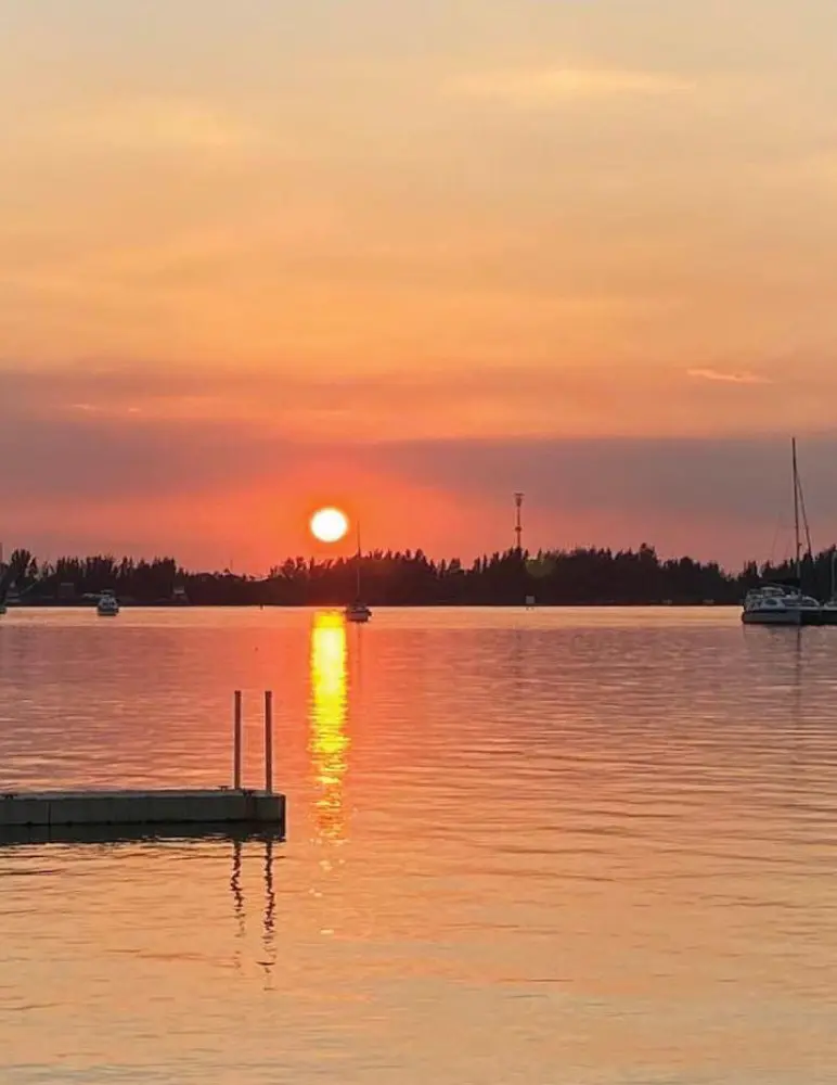 Sunset over a calm body of water with boats and a distant shoreline.