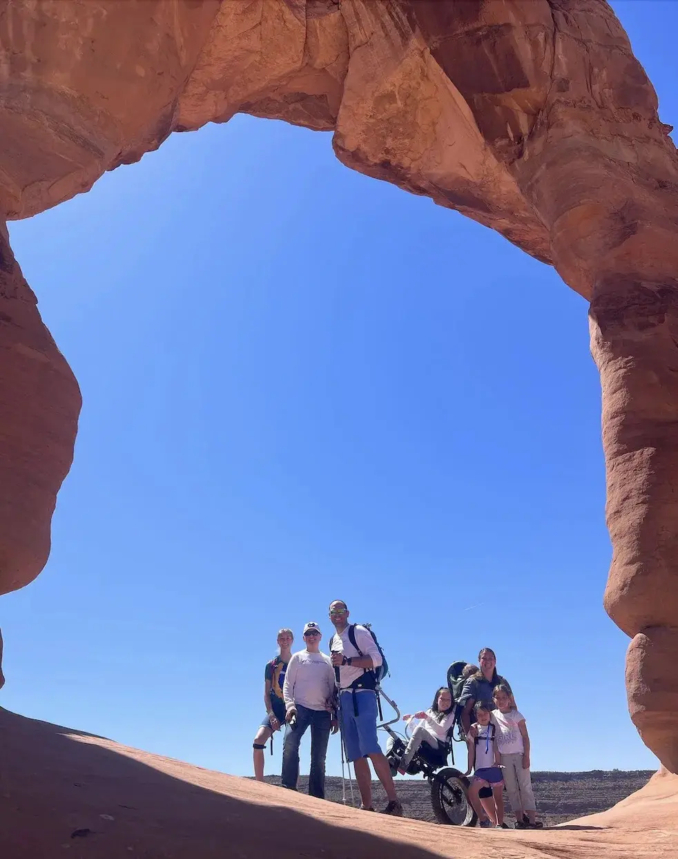 Group of people and a wheelchair under a large rock arch.