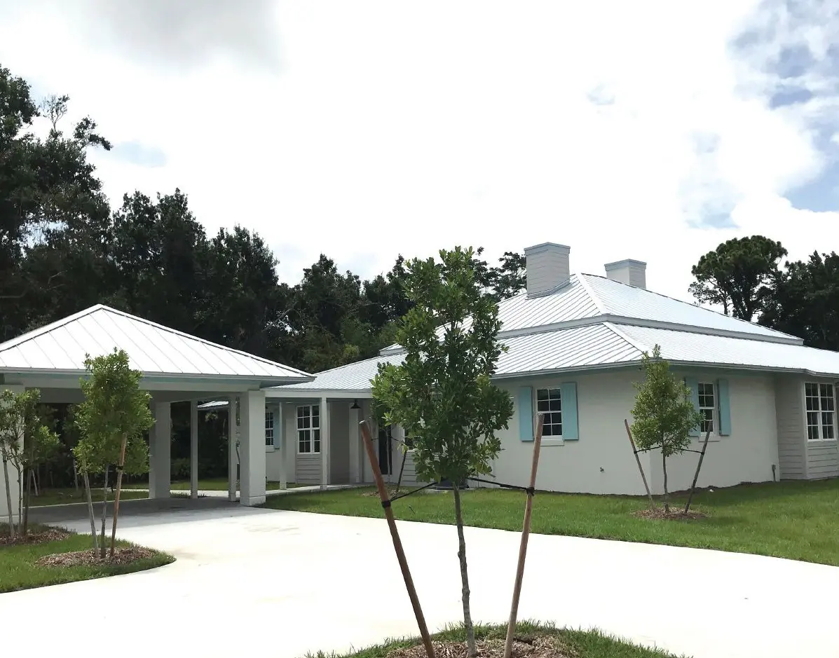 White house with a carport and trees in front.