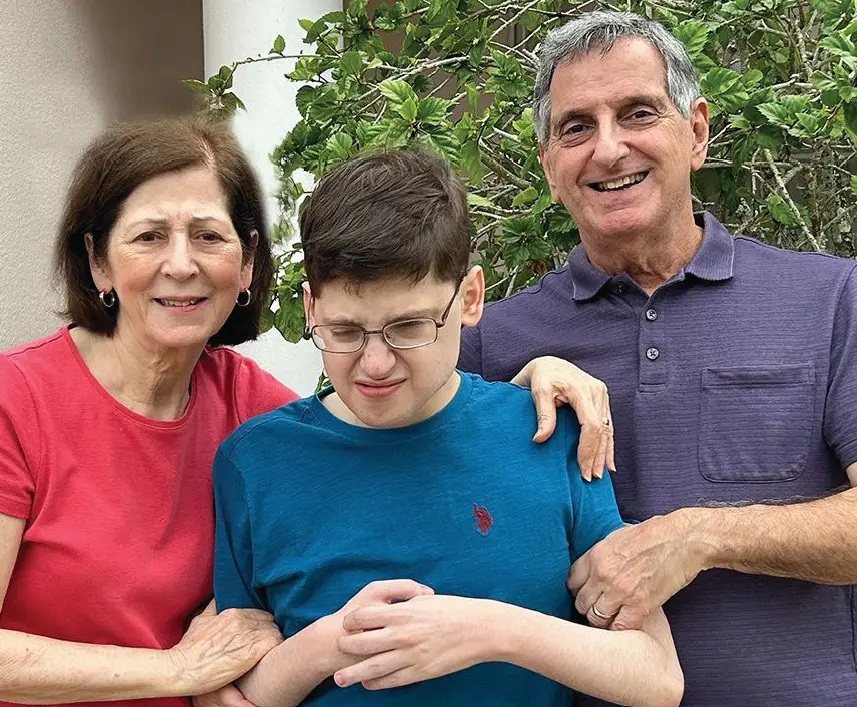 Three people smile for a photo in front of a plant.
