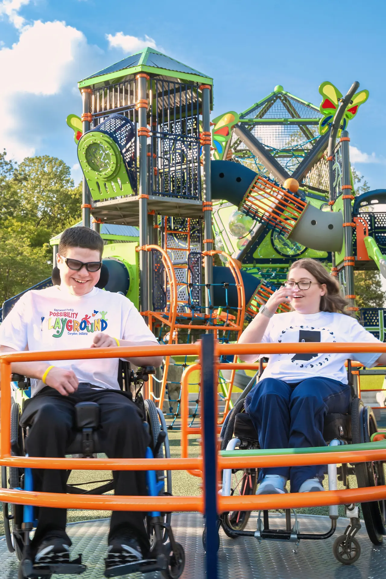 Two young people in wheelchairs smiling together at the accessible Possibility Playground in Corydon.
