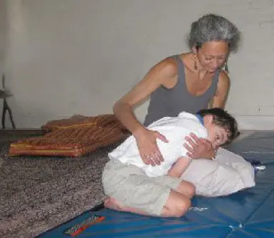 A mother comforting her son, Andreas, on a floor mat during a therapy session.