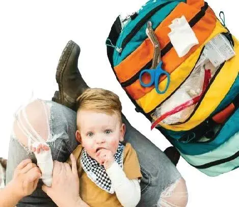 A baby sits on a person's lap next to a colorful TOBIQ bag filled with supplies.