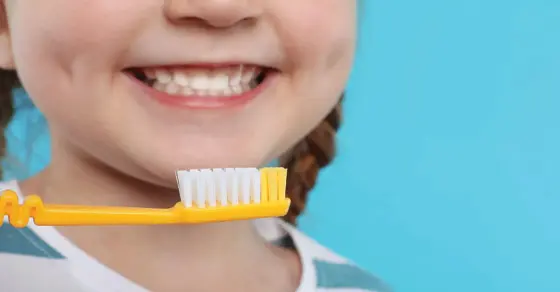 A child smiles with a yellow toothbrush in front of their mouth.