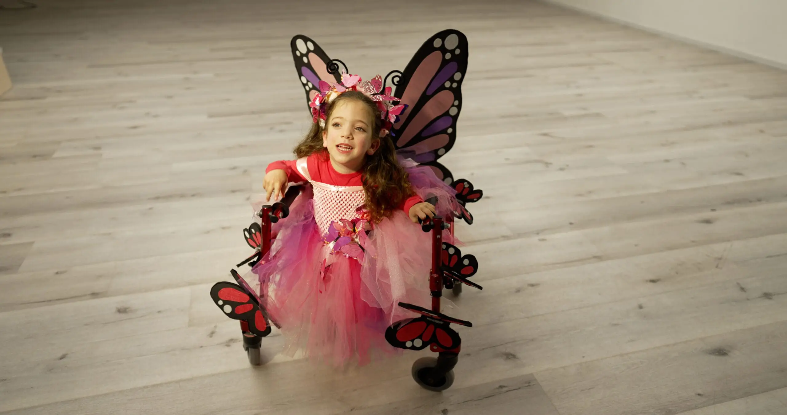 A young girl in a butterfly costume sits in a walker decorated with butterflies.