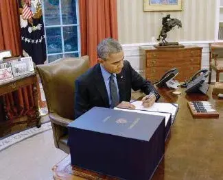 Barack Obama working at a desk in the Oval Office.
