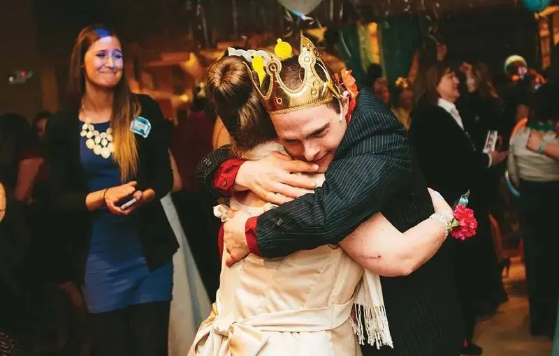 A man wearing a crown hugs a woman at a prom event.