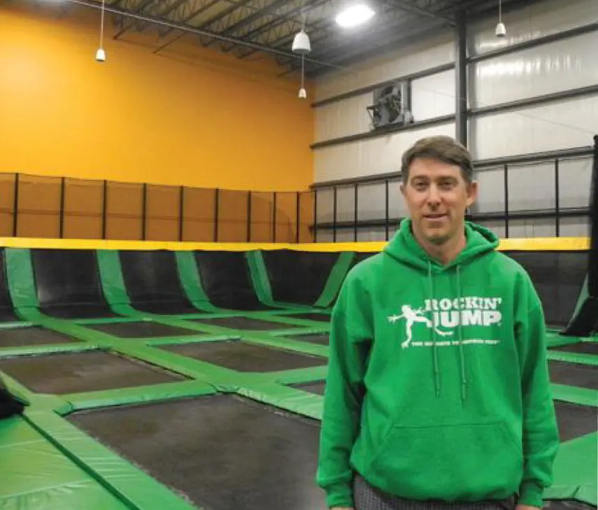 Man in a green Rockin' Jump hoodie standing in a trampoline park.