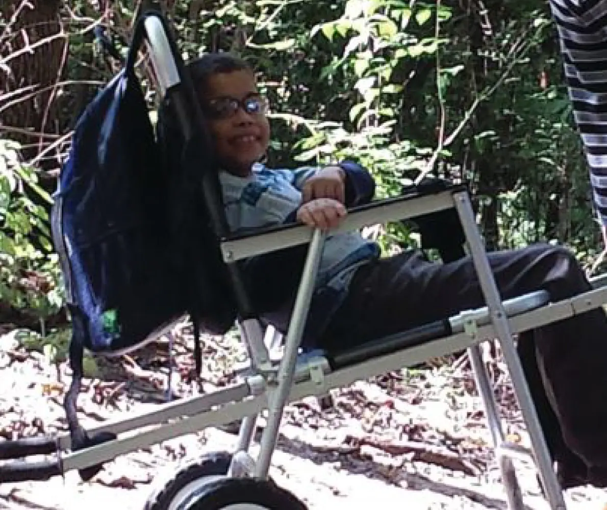 An 8-year-old boy smiles while sitting in a Freedom Chair outdoors.