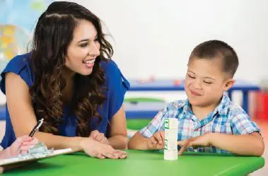 A woman and a young boy with Down syndrome interact at a table.