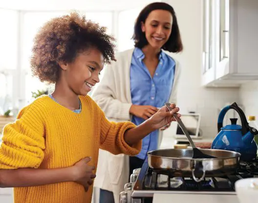 A child and an adult smile while cooking in a kitchen.