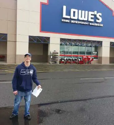 Man in a blue hoodie standing outside a Lowe's store.