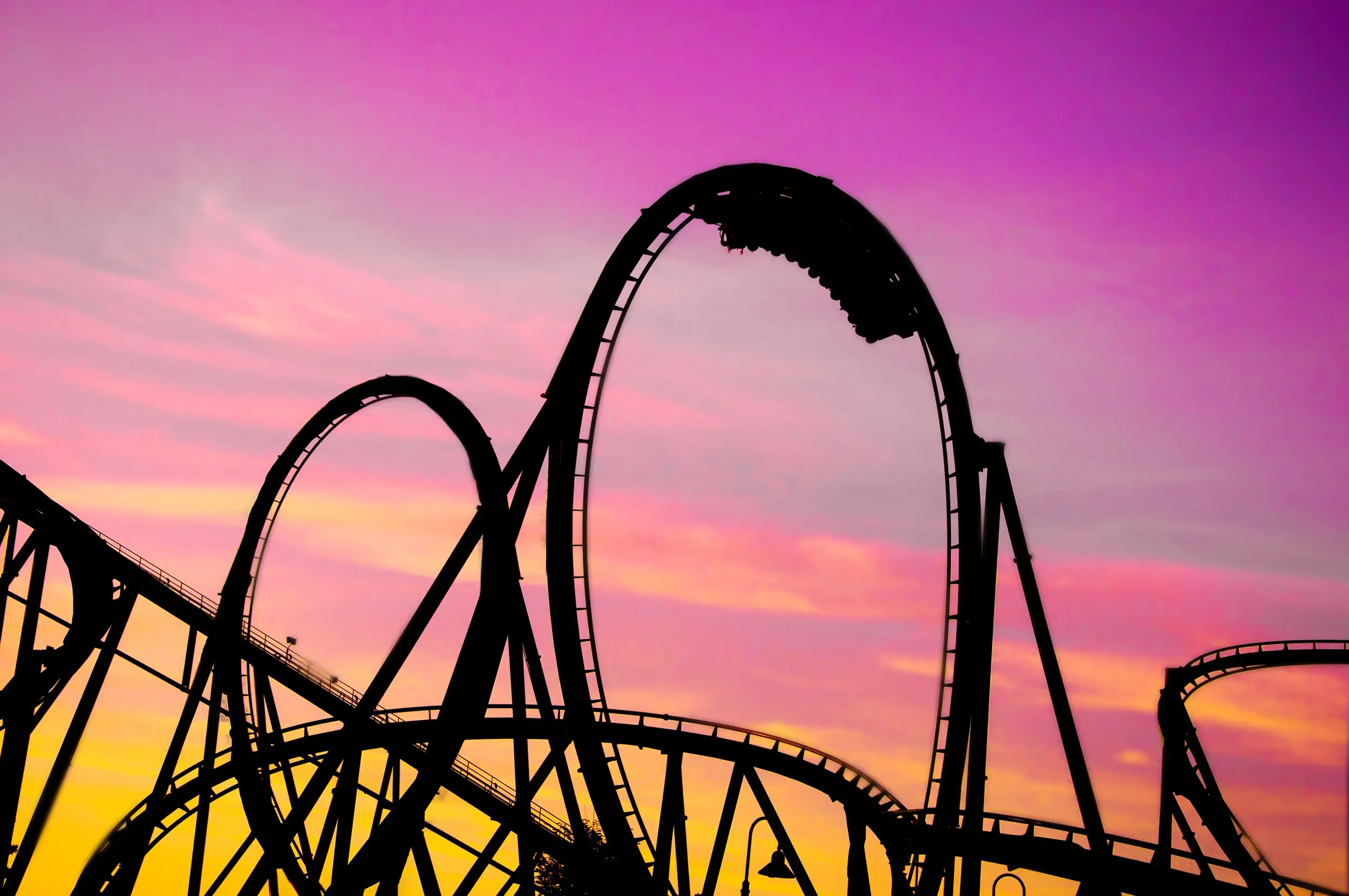 Silhouette of a roller coaster against a purple and orange sunset sky.