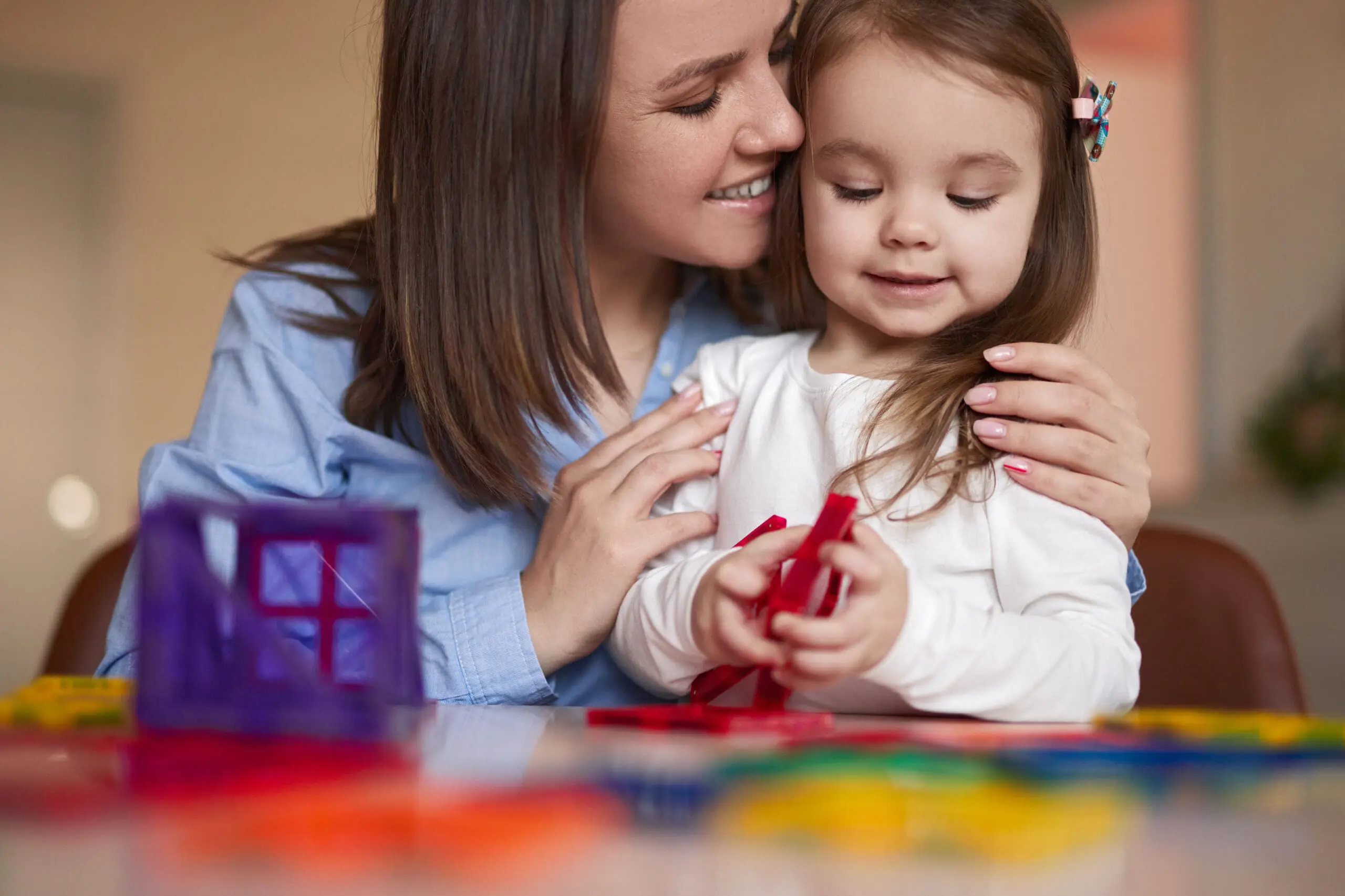 Mother and daughter building with colorful magnetic shapes together at a table.