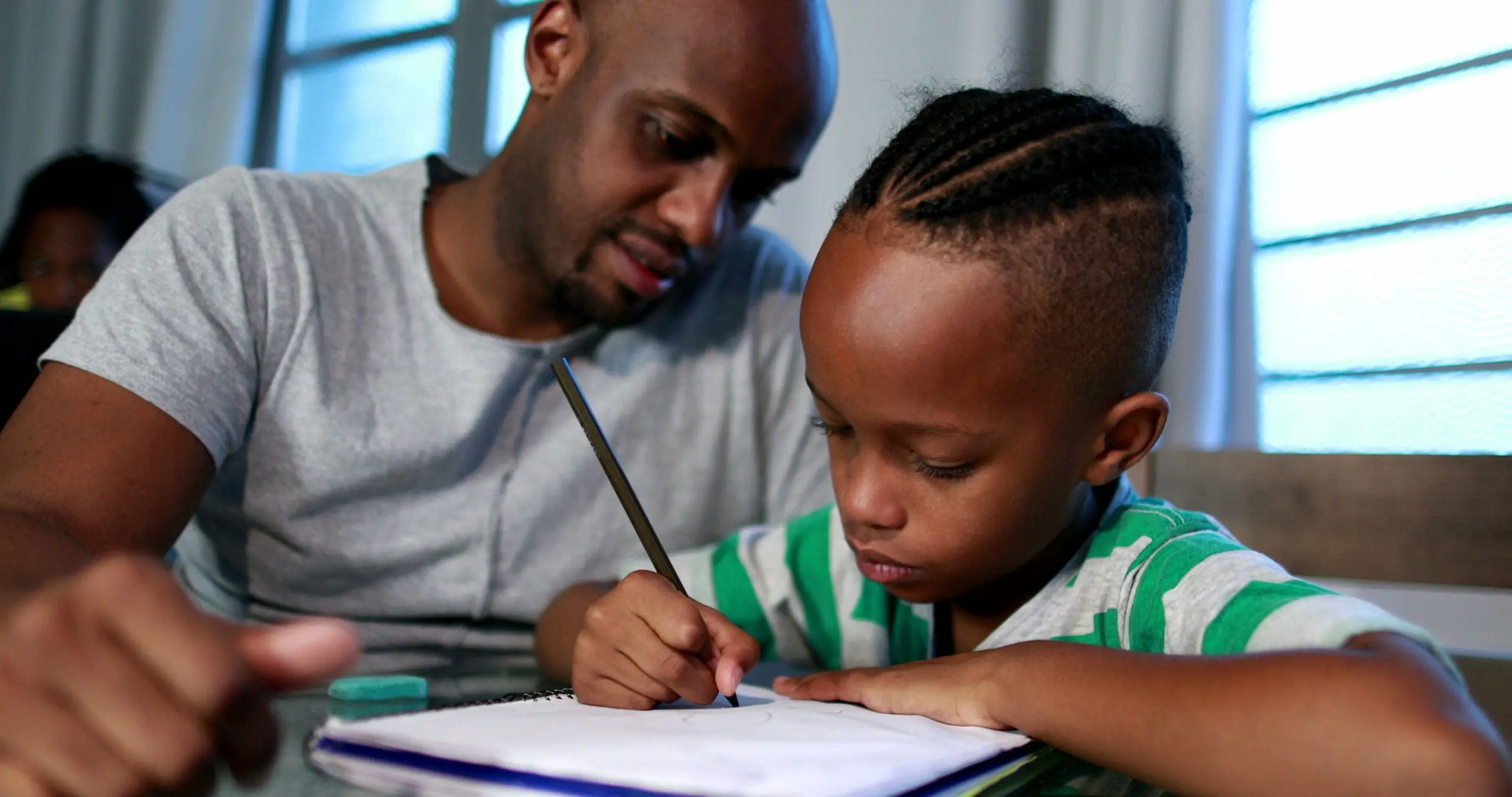 A man helps a young boy write in a notebook.