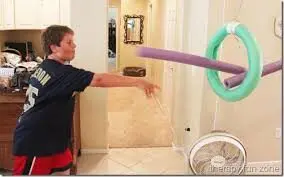 Boy throws a pool noodle to try and get it through a hanging ring.
