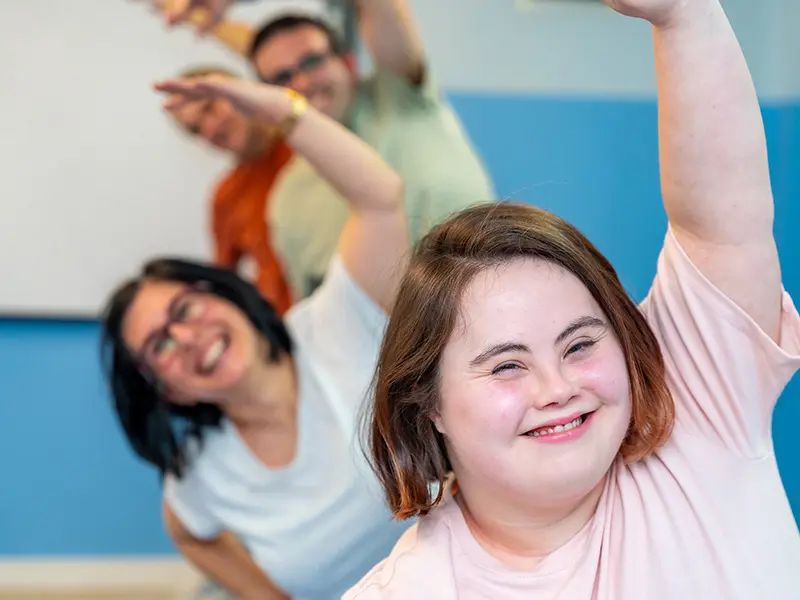 A group of people with Down syndrome doing yoga stretches indoors.
