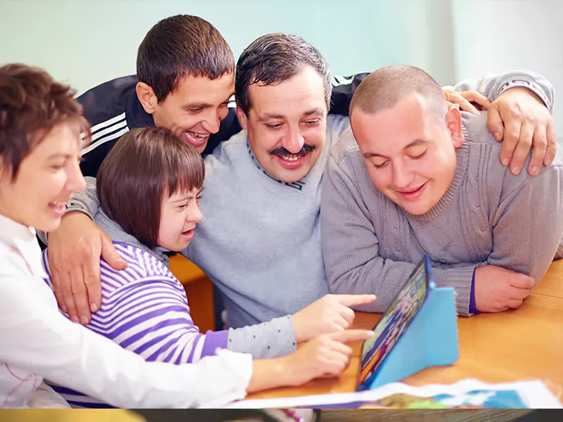 Five people gathered around a tablet on a table.
