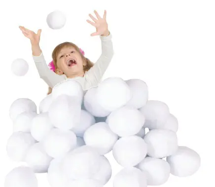 A young girl with arms raised is about to throw a snowball from a large pile of snowballs.