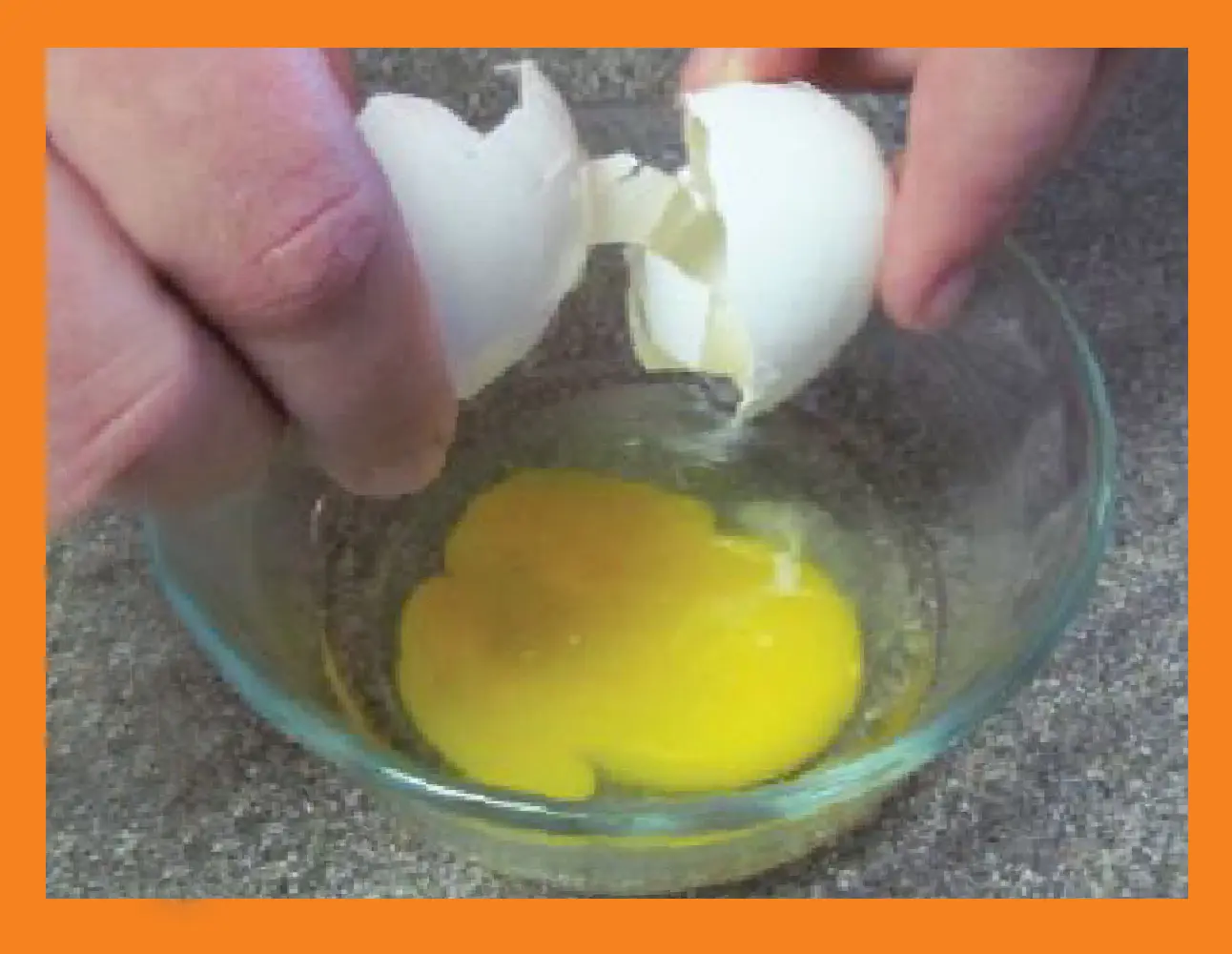 Hands cracking an egg into a glass bowl.