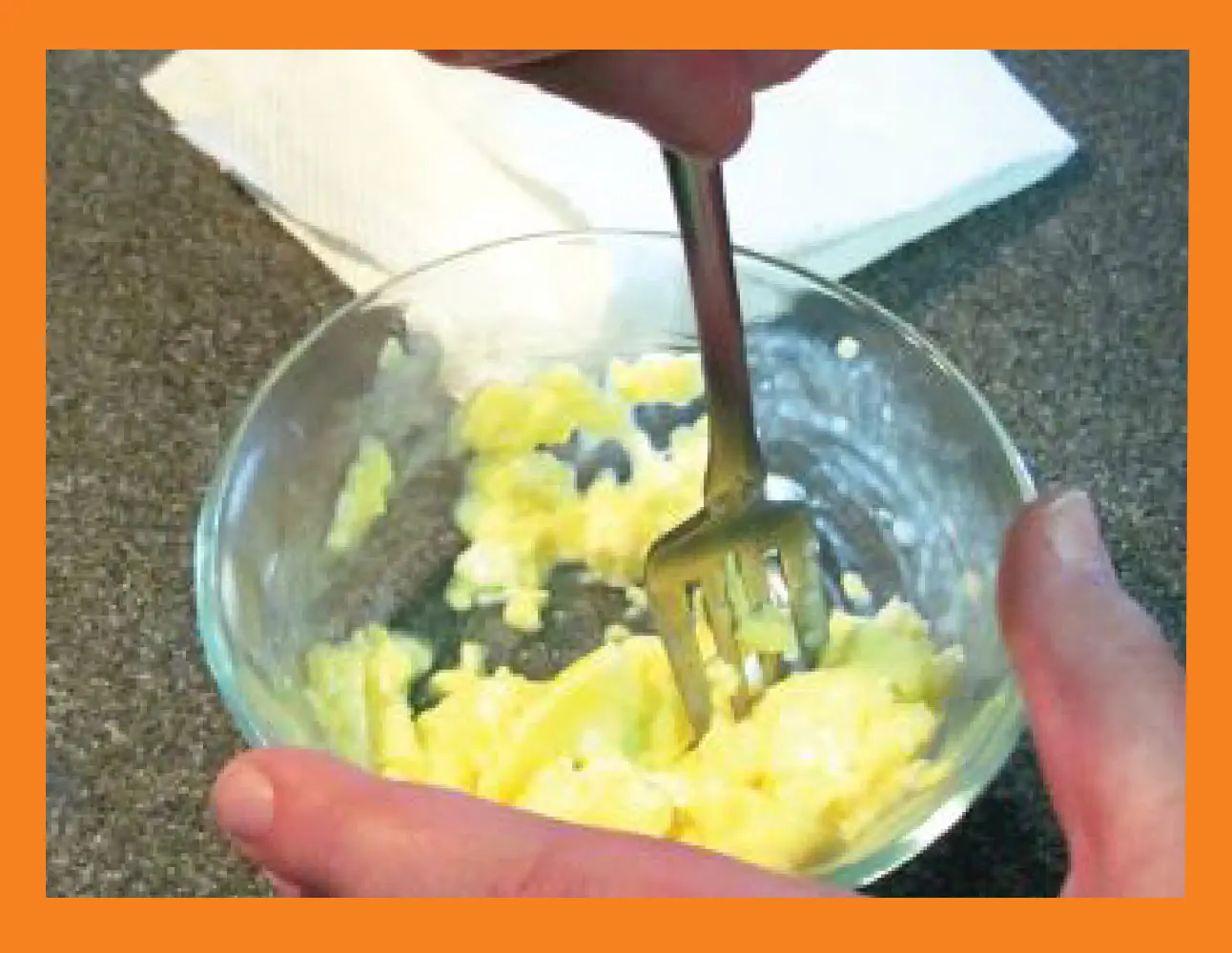 A fork stirs scrambled eggs in a clear bowl.