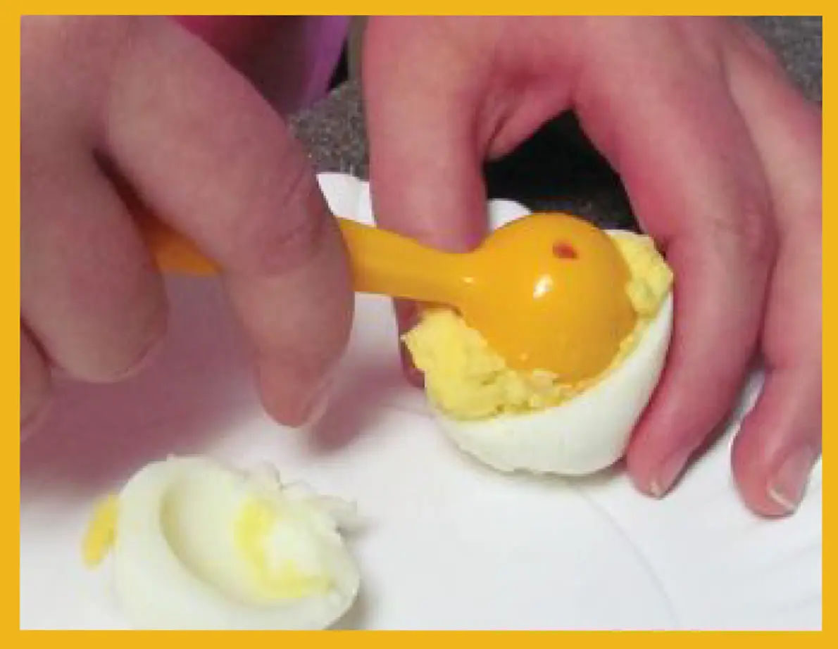 Hands scooping yolk from a hard-boiled egg with a yellow scooper.