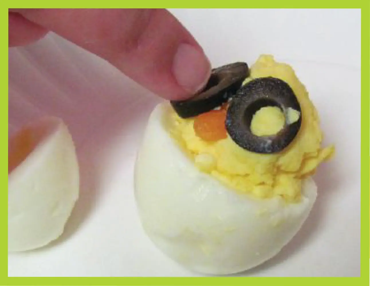 A finger places olive slices on a deviled egg to create a chick's eyes.