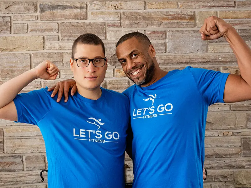 Keegan Johnson and Dante flex their arms while wearing matching blue "LET'S GO FITNESS" shirts.