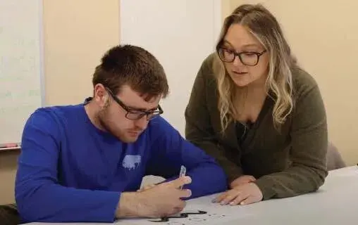 Norma Jean Miller works with a man at a table.