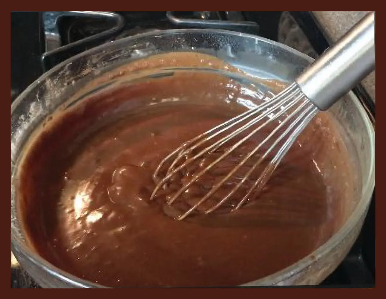 Whisk blending chocolate pudding in a glass bowl.