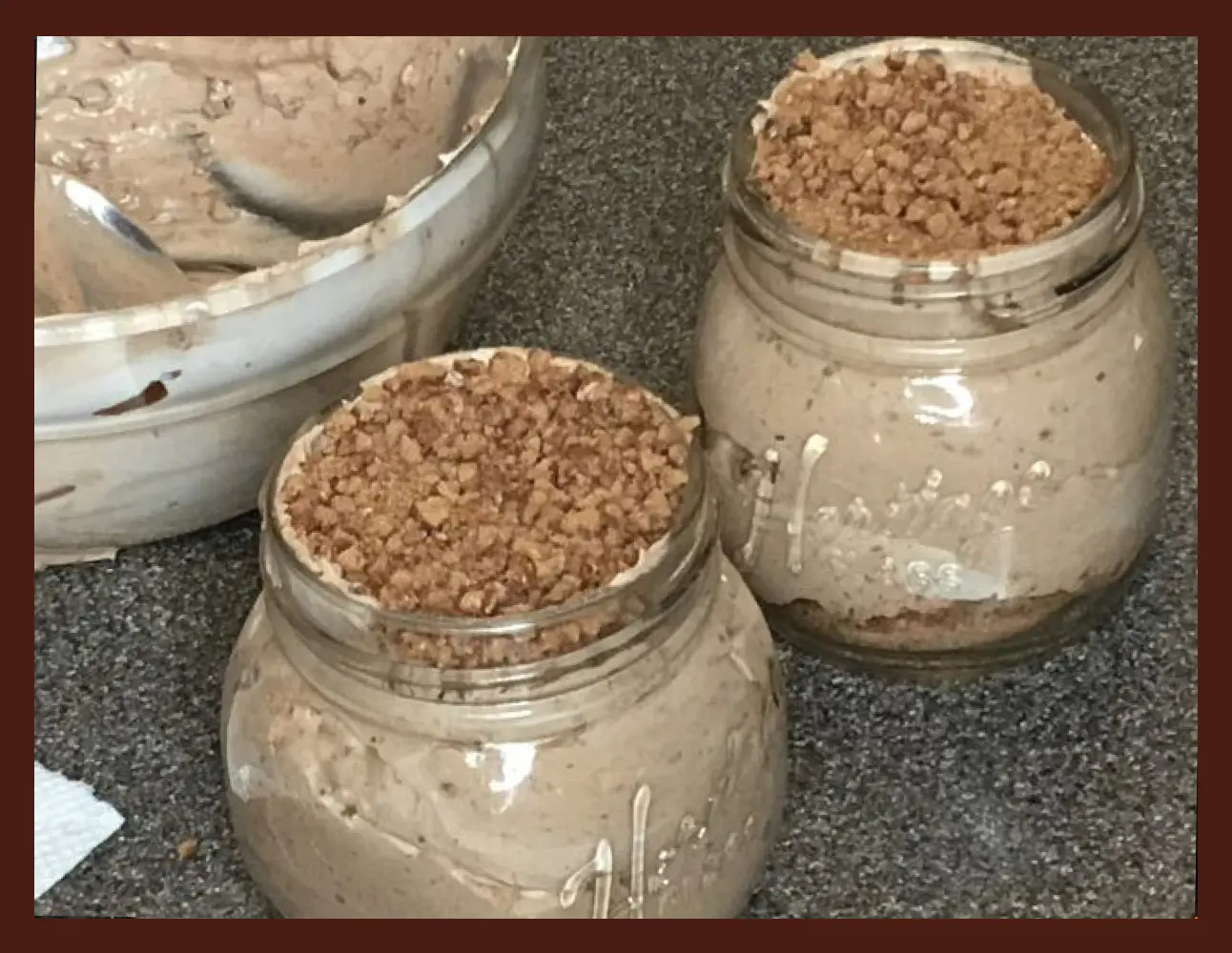 Two glass jars filled with chocolate pudding topped with crushed cookies, next to a bowl of pudding.