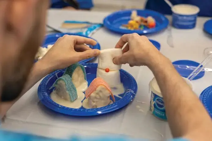 Hands decorating a mini ice cream cone village with frosting and candies.