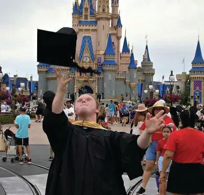 Nicholas McGee throws his graduation cap in the air in front of Cinderella Castle.