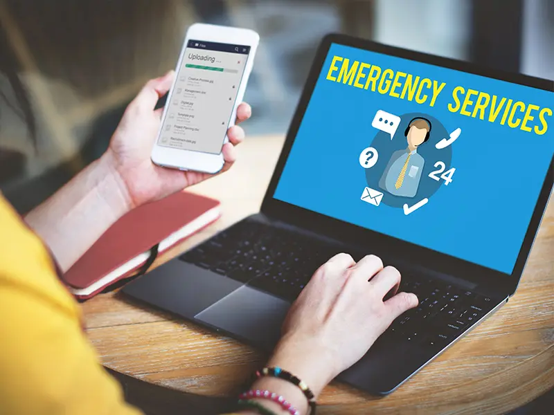 Person using a smartphone and laptop displaying emergency services information.