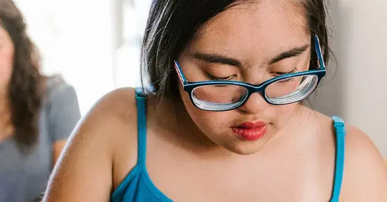 A young person wearing glasses looks down at a task.