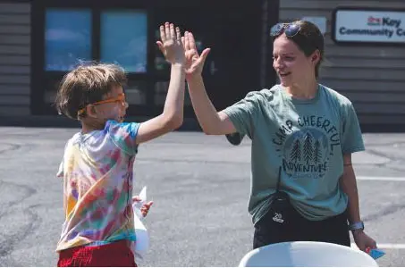Two children high-five in front of a building with a "Key Community" sign.