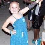 A smiling child in a blue dress with white snowflakes holds a bow and arrow.