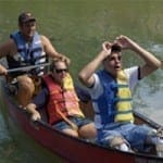 Three people in a canoe wearing life jackets enjoy a day on the water.