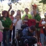 Group of happy children and young adults, some in a wheelchair, posing outdoors.