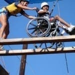 A counselor assists a child in a wheelchair on a suspended obstacle course.