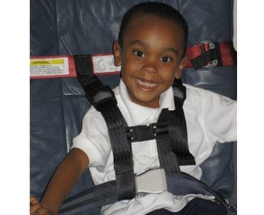 Smiling child secured in a CARES harness on an airplane.