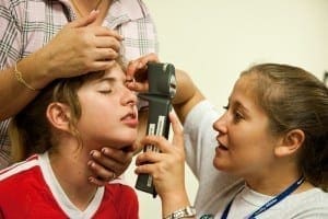 A healthcare professional examines a child's eye with a tool while an adult assists.