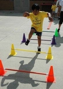Young athlete hurdles over a low bar during a Special Olympics event.