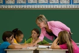 Teacher instructing students at desks in a classroom.
