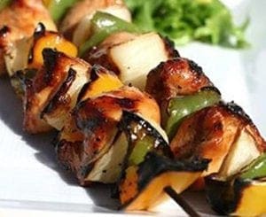 Chicken and vegetable skewers on a white plate.