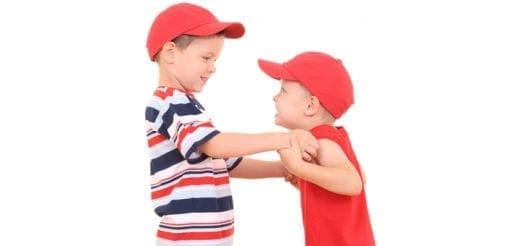 Two young boys in red caps face each other, one with his hands on the other's shoulders.