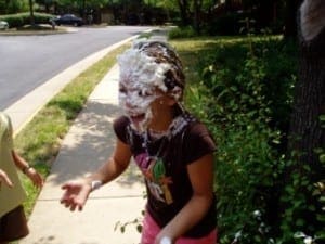 A person stands with their face covered in whipped cream and chocolate frosting.
