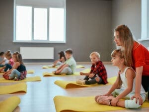 Instructor guiding children sitting on yoga mats in a bright studio.